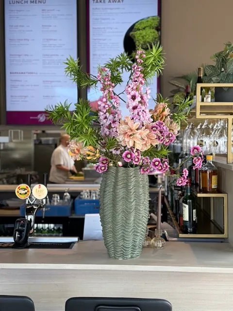 Há bleik blómaskreyting í grænum vasa á bar á veitingastað