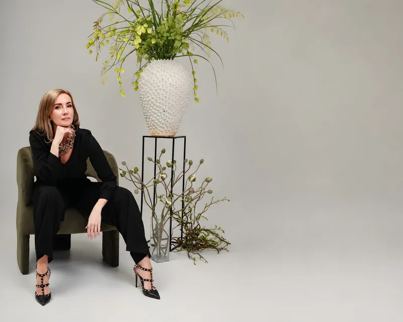 Ásta Björk Sigþórsdóttir, stofnandi Studio Bloom, situr í hægindastól við háa blómaskreytingu